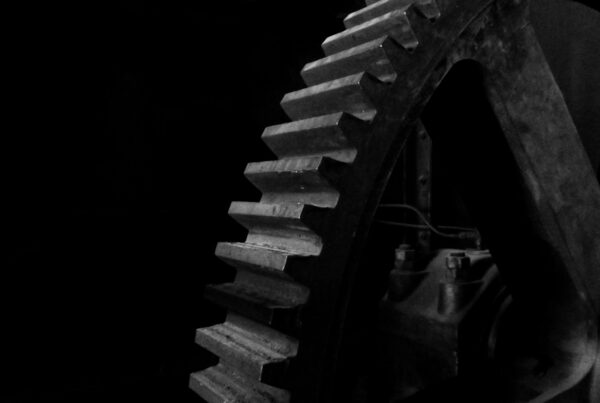 Machined steel gear teeth lit from the left against deep shadow