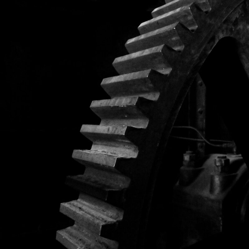 Machined steel gear teeth lit from the left against deep shadow