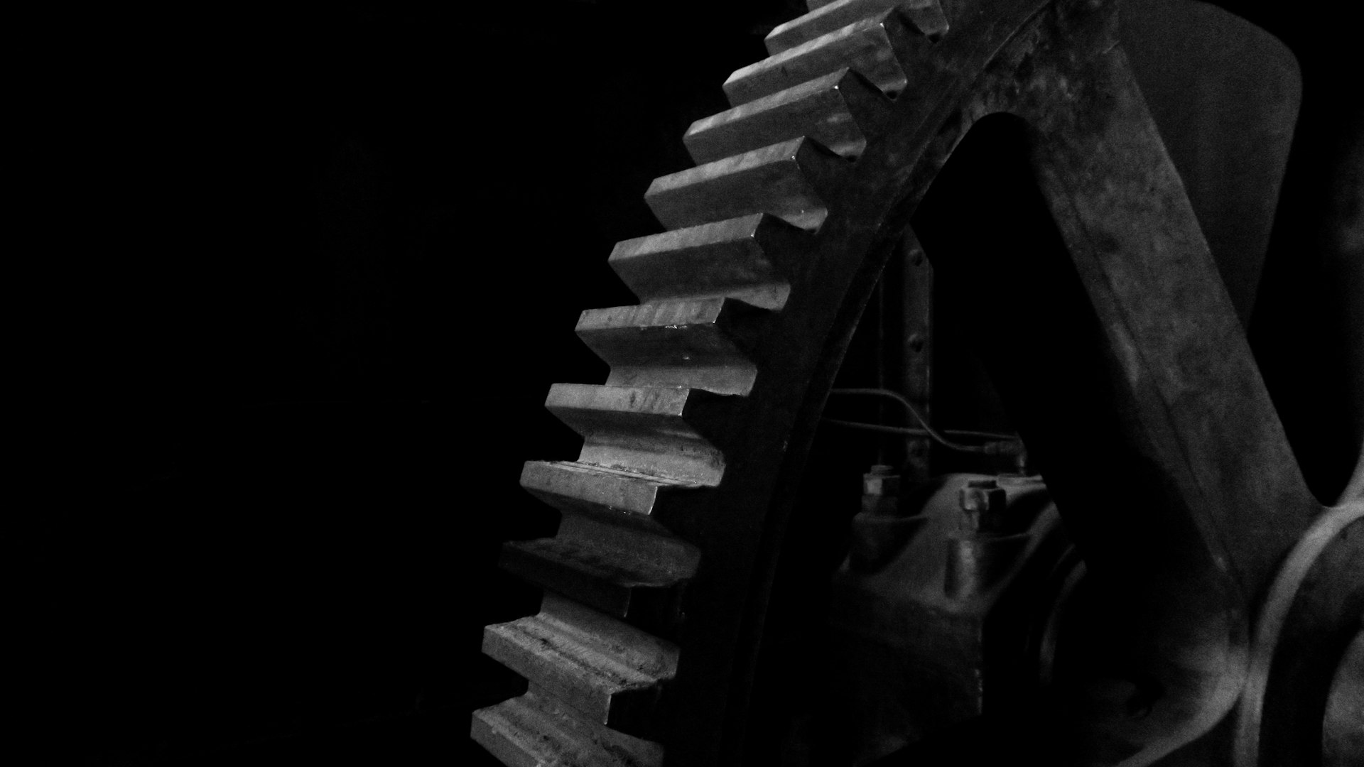 Machined steel gear teeth lit from the left against deep shadow