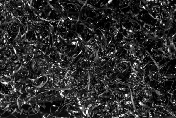 Dense pile of machined steel swarf lit hard from the left against darkness
