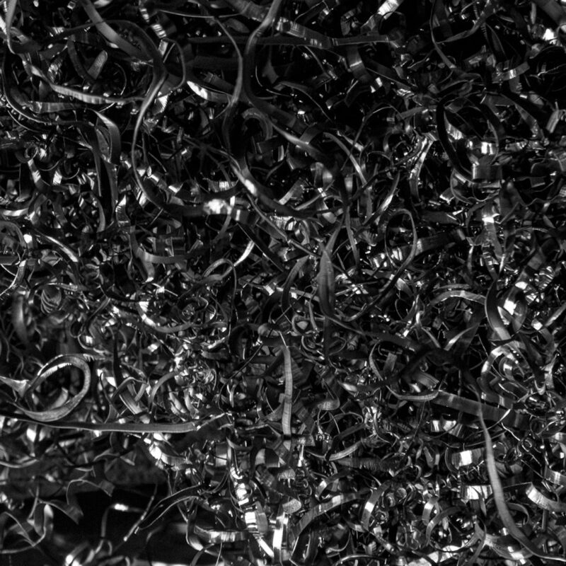 Dense pile of machined steel swarf lit hard from the left against darkness