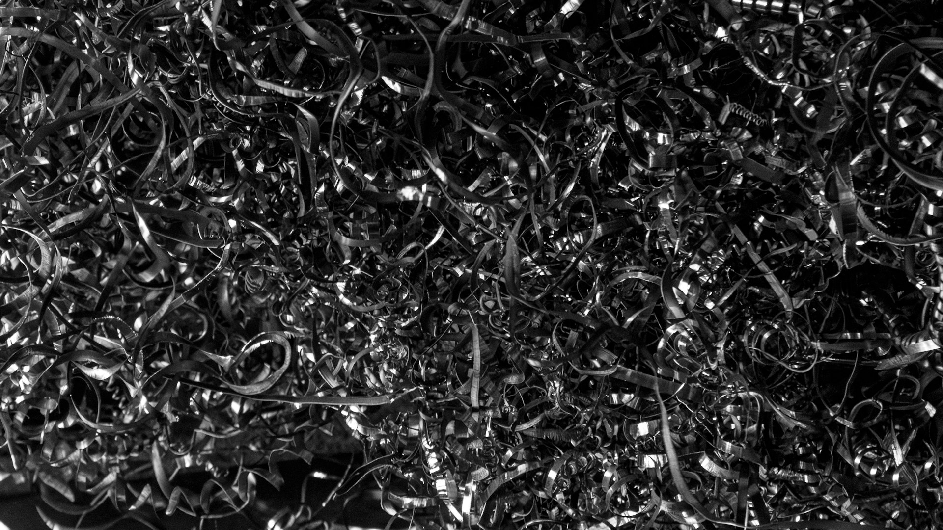 Dense pile of machined steel swarf lit hard from the left against darkness