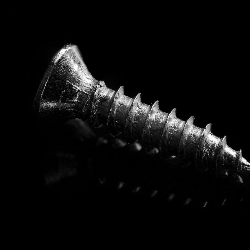 A single machined screw lit from the left against a matte black field