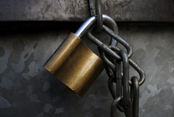 Brass padlock hanging on a steel chain against dark galvanized metal